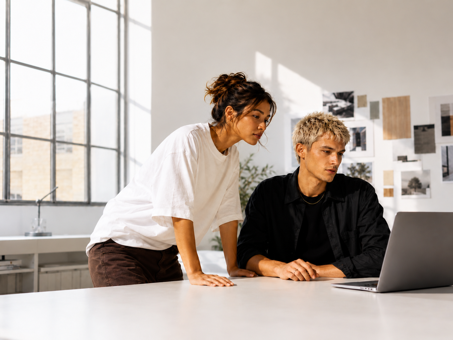 Two people collaborating at a desk with a laptop in a bright office.