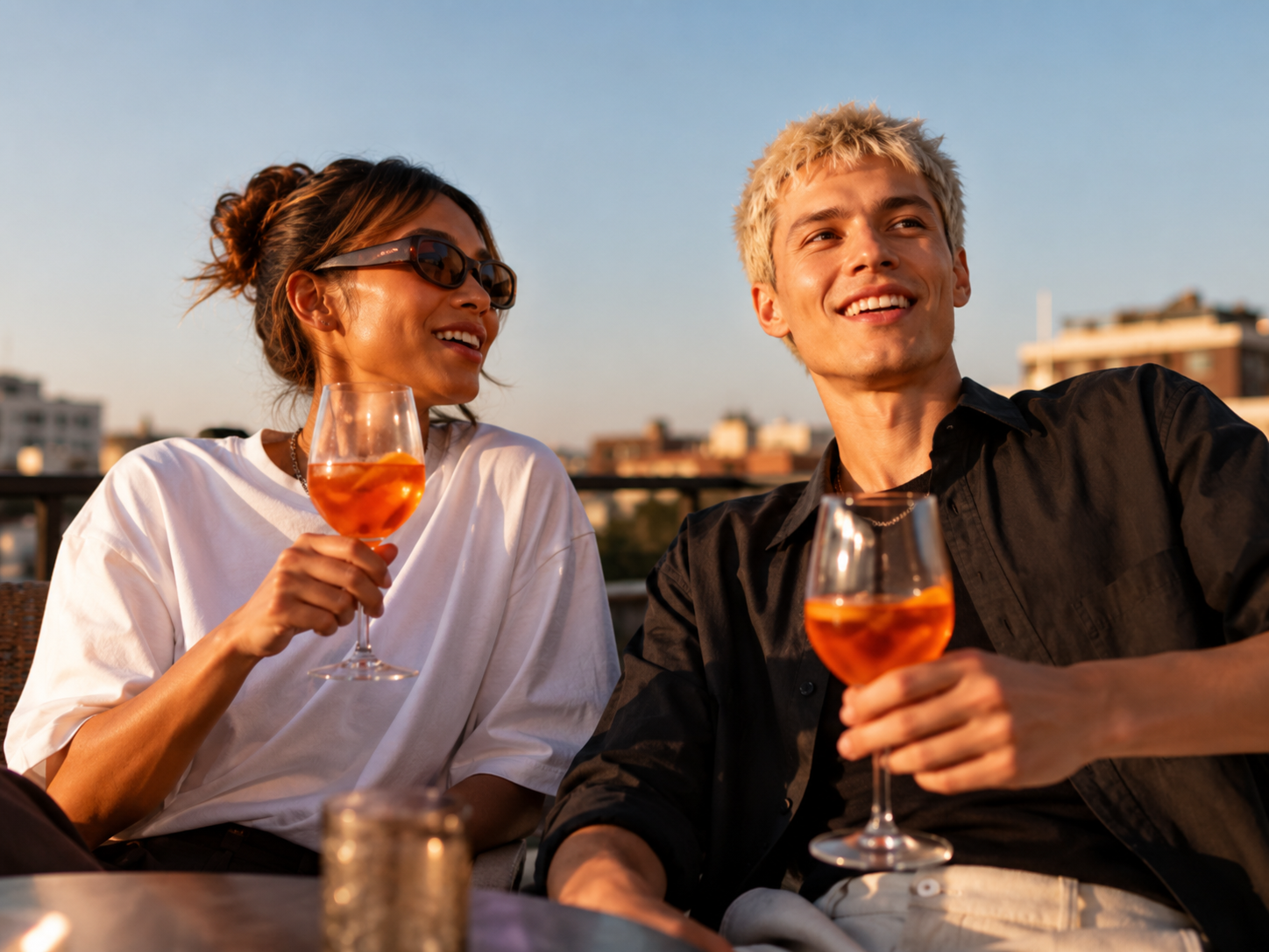 Two people enjoying drinks on a rooftop at sunset.