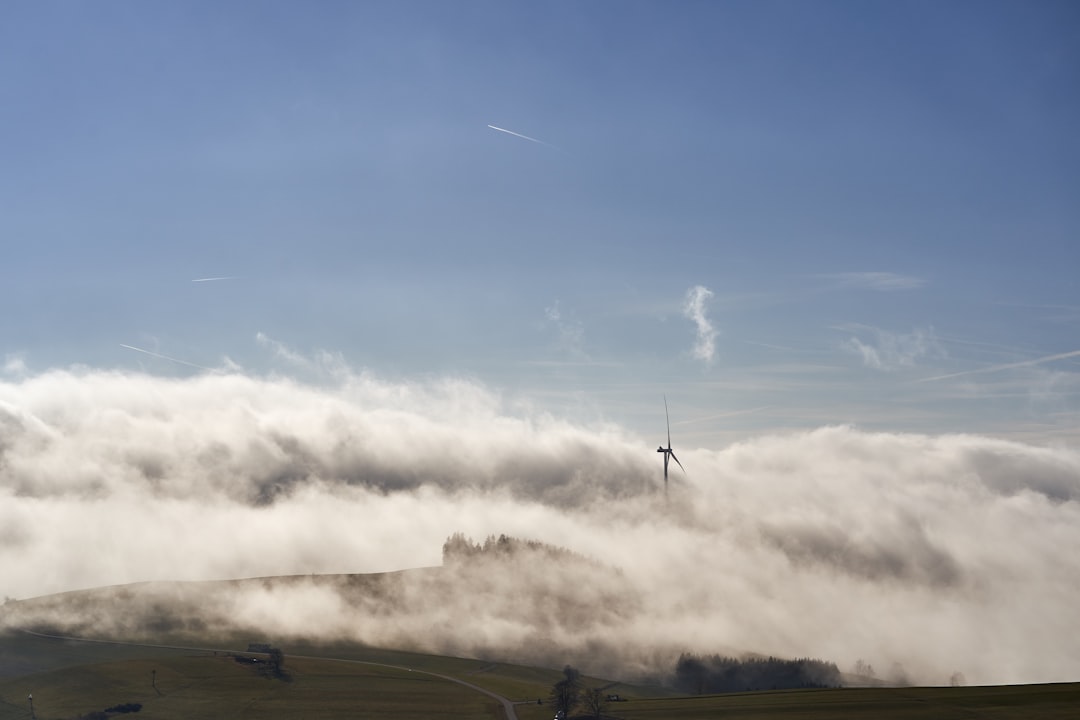 Wind turbine surrounded by clouds in a hilly landscape.