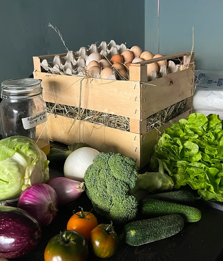Wooden crate of eggs surrounded by fresh vegetables.