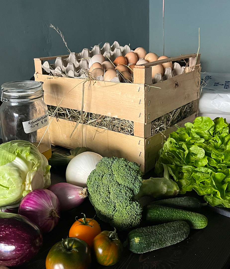Wooden crate of eggs surrounded by fresh vegetables.